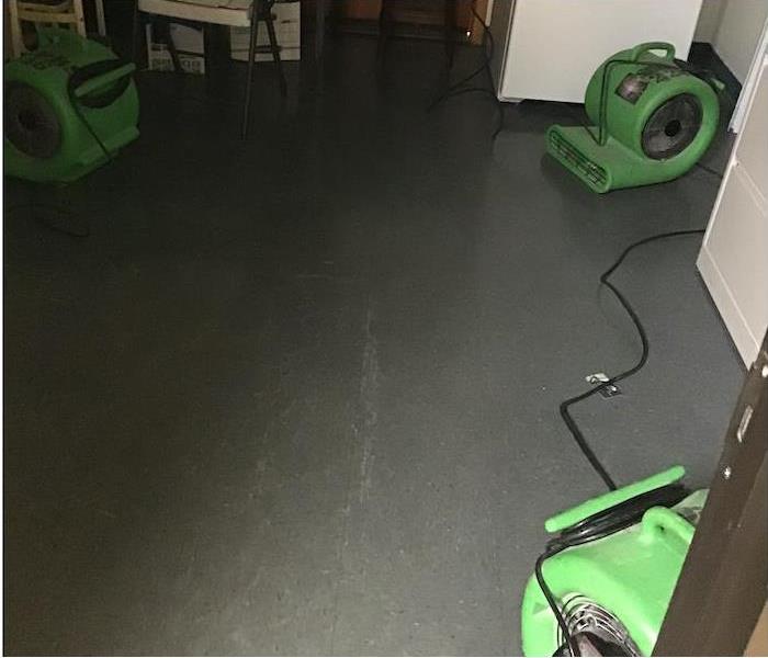Concrete floor and a small refrigerator in the background as three air movers complete the drying process