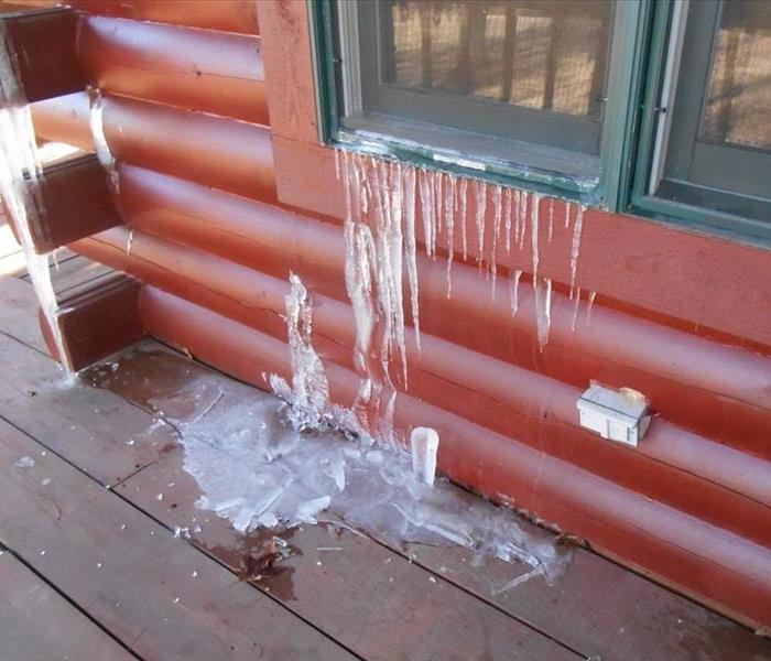 Icicles hanging down from a window of a red log cabin