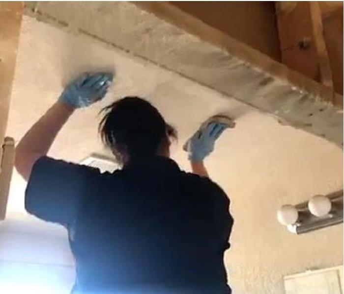 Female technician wearing a black shirt and blue gloves cleaning soot on a ceiling