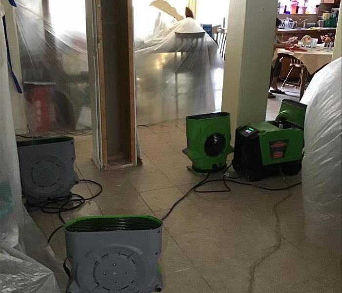 Plastic sheeting covers furniture in a living room with SERVPRO green air movers strategically placed in a home