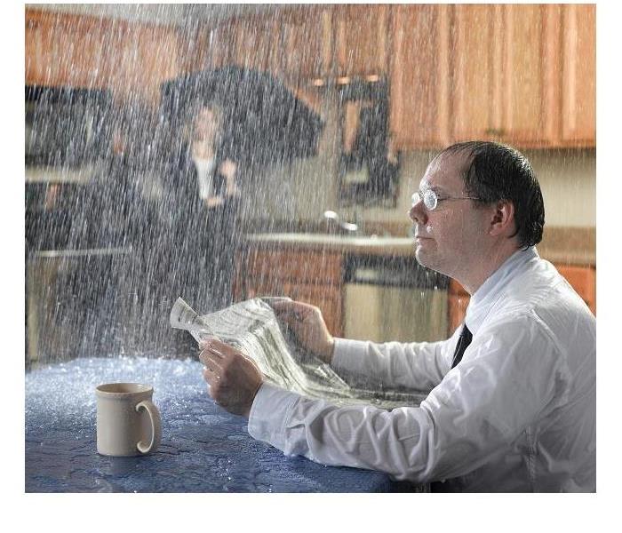 Rain falling through the ceiling in a kitchen while a man is reading the newspaper and having his coffee