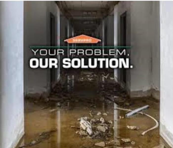 Flooding in a hallway with debris. SERVPRO House that says Your Problem. Our Solution. under it