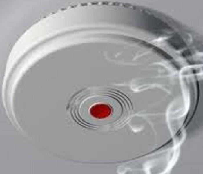 White smoke detector with red button and smoke going towards it