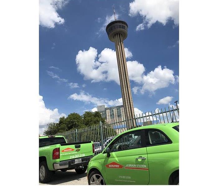 A SERVPRO green truck and green car parked near the Tower of The Americas