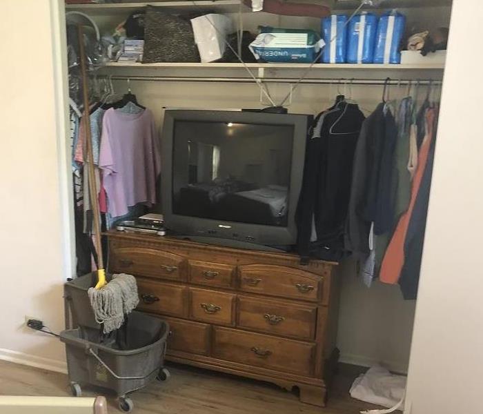 TV and clothes in a closet, mop in front of the dresser drawers