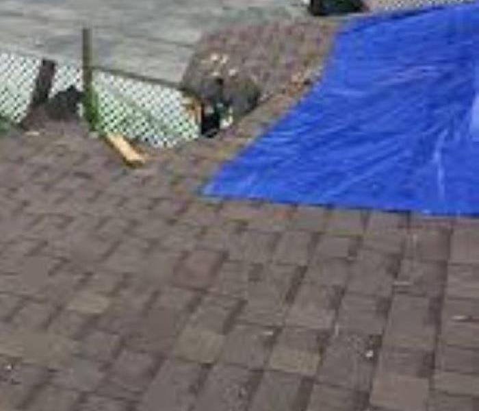 Storm damaged roof with a blue tarp on top