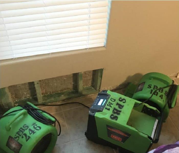 Three pieces of green drying equipment including a dehumidifier and air movers in a home with flood cuts on the wall